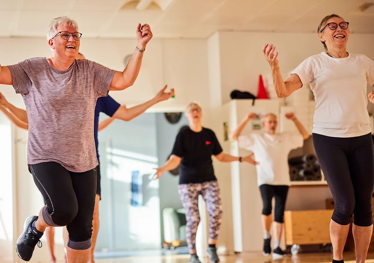 Lächelnde Gruppe von Senioren, die einen Fitnesskurs in einem Fitnessstudio machen